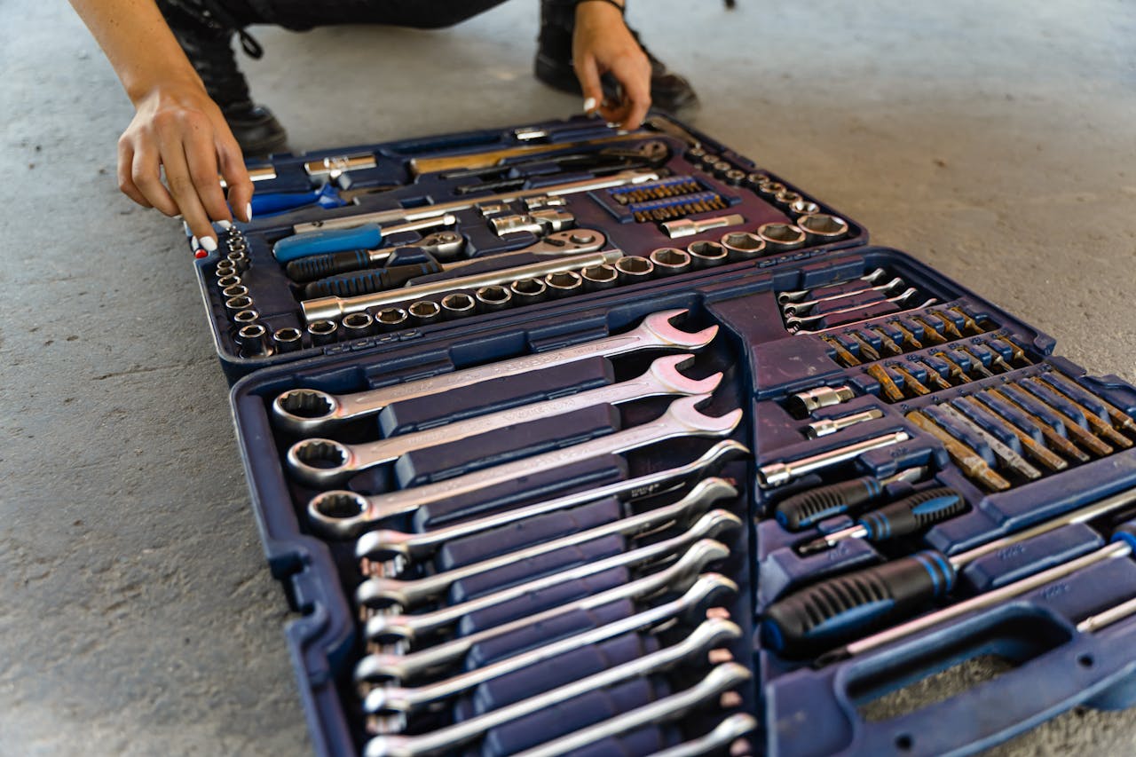 our-story Close-up view of an open toolbox on a concrete floor, displaying various hand tools including wrenches, screwdrivers, and socket sets.
